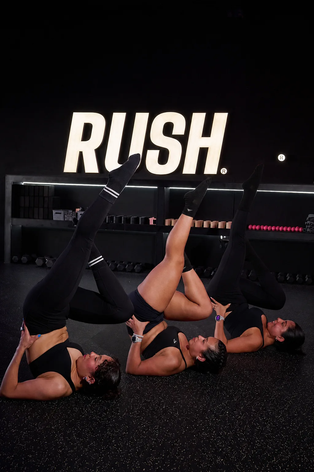 Tres Rushers en el suelo del RUSH Room bajo el letrero iluminado, moviéndose al mismo tiempo